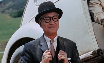 Movie still from “The Love Bug” (1969), directed by Robert Stevenson – A man in a suit and hat is putting on his tie; Close Up shot, Low angle