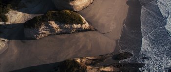Movie still from “The Lovely Bones” (2009), directed by Peter Jackson – A person walking on a beach near a body of water; Extreme Wide shot, Overhead angle