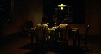 Movie still from “The Lover” (1992), directed by Jean-Jacques Annaud – A group of people sitting at a table in the dark; Wide shot, High angle