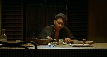 Movie still from “The Lover” (1992), directed by Jean-Jacques Annaud – A man sitting at a table with a plate in front of him; Medium shot, Low angle