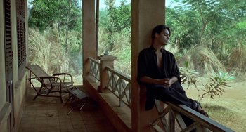 Movie still from “The Lover” (1992), directed by Jean-Jacques Annaud – A man sitting on top of a bench near a window; Wide shot, High angle