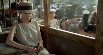 Movie still from “The Lover” (1992), directed by Jean-Jacques Annaud – A woman sitting on a train with a hat on; Medium shot, Over the shoulder angle