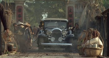 Movie still from “The Lover” (1992), directed by Jean-Jacques Annaud – An old car parked on the side of the road; Wide shot, Over the shoulder angle