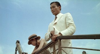 Movie still from “The Lover” (1992), directed by Jean-Jacques Annaud – A man and a woman standing next to a railing; Medium shot, Low angle