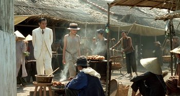 Movie still from “The Lover” (1992), directed by Jean-Jacques Annaud – A group of people standing next to each other in front of a grill; Wide shot, Over the shoulder angle