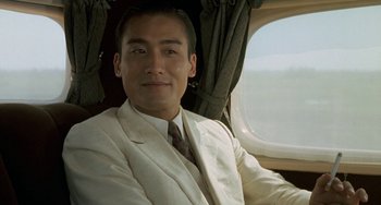 Movie still from “The Lover” (1992), directed by Jean-Jacques Annaud – A man in a suit and tie sitting in a plane; Close Up shot, Low angle