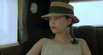 Movie still from “The Lover” (1992), directed by Jean-Jacques Annaud – A woman wearing a hat with a braid in her hair; Close Up shot, Over the shoulder angle