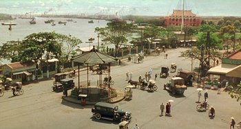 Movie still from “The Lover” (1992), directed by Jean-Jacques Annaud – An old photo of a street scene with cars and horses; Extreme Wide shot, High angle