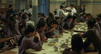 Movie still from “The Lover” (1992), directed by Jean-Jacques Annaud – A group of people sitting at a table eating food; Wide shot, High angle