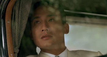 Movie still from “The Lover” (1992), directed by Jean-Jacques Annaud – A person wearing a suit and holding an umbrella; Close Up shot, Low angle