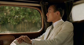 Movie still from “The Lover” (1992), directed by Jean-Jacques Annaud – A man sitting in a car looking out the window; Close Up shot, Over the shoulder angle