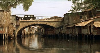 Movie still from “The Lover” (1992), directed by Jean-Jacques Annaud – A bridge over a body of water with a car on it; Extreme Wide shot, High angle
