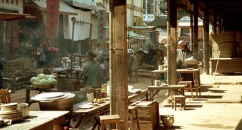 Movie still from “The Lover” (1992), directed by Jean-Jacques Annaud – A group of people standing around tables in an open air market; Wide shot, High angle