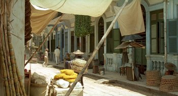 Movie still from “The Lover” (1992), directed by Jean-Jacques Annaud – A street scene with people walking on the sidewalk; Extreme Wide shot, High angle