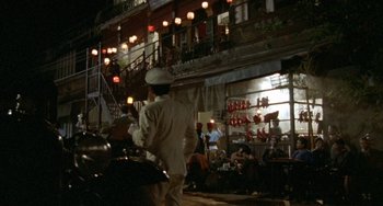 Movie still from “The Lover” (1992), directed by Jean-Jacques Annaud – A man in a white suit and a white hat is walking down the street; Extreme Wide shot, High angle