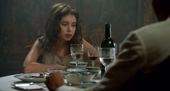 Movie still from “The Lover” (1992), directed by Jean-Jacques Annaud – A woman sitting at a dinner table with wine glasses; Close Up shot, Over the shoulder angle