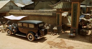 Movie still from “The Lover” (1992), directed by Jean-Jacques Annaud – An old car parked in front of an old building; Wide shot, High angle