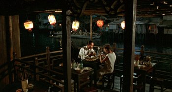 Movie still from “The Lover” (1992), directed by Jean-Jacques Annaud – A man and a woman sitting at a table; Wide shot, High angle
