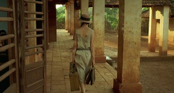 Movie still from “The Lover” (1992), directed by Jean-Jacques Annaud – A woman walking down a walkway holding a suitcase; Wide shot, Over the shoulder angle