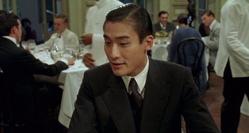 Movie still from “The Lover” (1992), directed by Jean-Jacques Annaud – A man wearing a suit and tie sitting at a table in a restaurant; Close Up shot, Over the shoulder angle