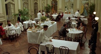 Movie still from “The Lover” (1992), directed by Jean-Jacques Annaud – People are sitting at tables in a restaurant; Extreme Wide shot, High angle
