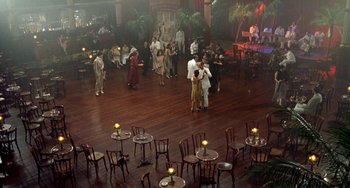 Movie still from “The Lover” (1992), directed by Jean-Jacques Annaud – A group of people standing in a large room; Extreme Wide shot, High angle