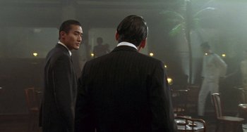 Movie still from “The Lover” (1992), directed by Jean-Jacques Annaud – Two men in suits are standing in front of a mirror; Medium shot, Over the shoulder angle