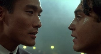 Movie still from “The Lover” (1992), directed by Jean-Jacques Annaud – Two men face to face in a dark room; Close Up shot, Over the shoulder angle