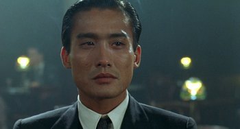 Movie still from “The Lover” (1992), directed by Jean-Jacques Annaud – A person wearing a suit and tie; Close Up shot, Low angle