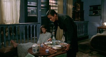 Movie still from “The Lover” (1992), directed by Jean-Jacques Annaud – A man and a little girl standing at a dining table; Medium shot, High angle