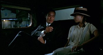 Movie still from “The Lover” (1992), directed by Jean-Jacques Annaud – A man and a woman sitting in the back of a car; Medium shot, Over the shoulder angle