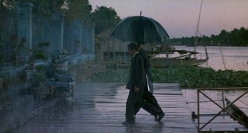 Movie still from “The Lover” (1992), directed by Jean-Jacques Annaud – A man walking down the street holding an umbrella; Wide shot, High angle