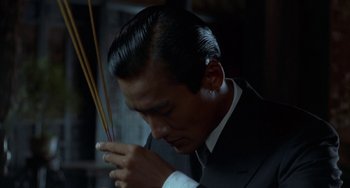 Movie still from “The Lover” (1992), directed by Jean-Jacques Annaud – A man in a suit and tie holding a pair of chopsticks; Close Up shot, Low angle