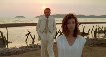 Movie still from “The Lover” (1992), directed by Jean-Jacques Annaud – A man and a woman standing next to each other on a beach; Medium shot, Over the shoulder angle