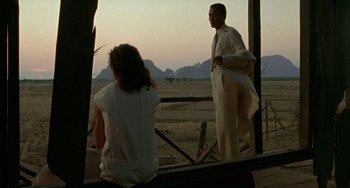 Movie still from “The Lover” (1992), directed by Jean-Jacques Annaud – A man and a woman standing in front of an open gate; Wide shot, Over the shoulder angle