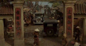 Movie still from “The Lover” (1992), directed by Jean-Jacques Annaud – An old car is parked in a dirt lot; Extreme Wide shot, High angle