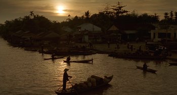 Movie still from “The Lover” (1992), directed by Jean-Jacques Annaud – A group of people on small boats in a body of water at sunset; Extreme Wide shot, High angle