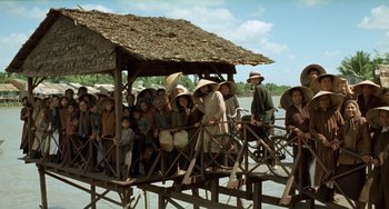 Movie still from “The Lover” (1992), directed by Jean-Jacques Annaud – A group of people sitting on top of a wooden platform; Extreme Wide shot, High angle