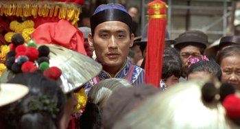 Movie still from “The Lover” (1992), directed by Jean-Jacques Annaud – A man wearing a blue hat and a blue robe; Close Up shot, Over the shoulder angle