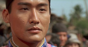 Movie still from “The Lover” (1992), directed by Jean-Jacques Annaud – A man's face in front of a group of people; Close Up shot, Low angle