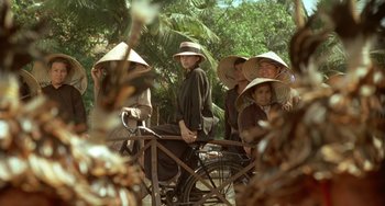 Movie still from “The Lover” (1992), directed by Jean-Jacques Annaud – A group of people sitting on top of a bike; Wide shot, Over the shoulder angle