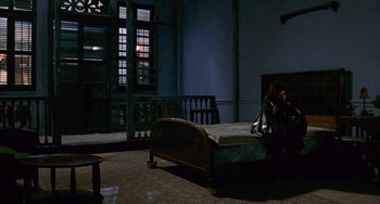 Movie still from “The Lover” (1992), directed by Jean-Jacques Annaud – A woman sitting on a bed in a dark room; Wide shot, High angle
