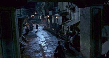 Movie still from “The Lover” (1992), directed by Jean-Jacques Annaud – People walking down a street at night in the dark; Extreme Wide shot, High angle