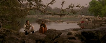 Movie still from “The Lovers” (2015), directed by Roland Joffé – A woman sitting on a rock near a body of water; Wide shot, High angle