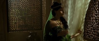 Movie still from “The Lovers” (2015), directed by Roland Joffé – A woman dressed in a green dress and a gold necklace; Medium shot, Over the shoulder angle