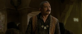 Movie still from “The Lovers” (2015), directed by Roland Joffé – An older man with a mustache wearing a necklace; Close Up shot, Over the shoulder angle