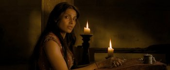 Movie still from “The Lovers” (2015), directed by Roland Joffé – A woman sitting in front of a lit candle in a room; Medium shot, Over the shoulder angle