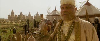 Movie still from “The Lovers” (2015), directed by Roland Joffé – An old man with a long beard wearing a crown and standing in front of a group of people; Medium shot, Low angle