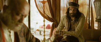Movie still from “The Lovers” (2015), directed by Roland Joffé – A man sitting on a chair in a room; Medium shot, Over the shoulder angle