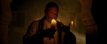 Movie still from “The Lovers” (2015), directed by Roland Joffé – An old man holding a candle in a dark room; Medium shot, Low angle